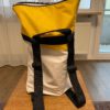 Ein Rucksack bestehend aus den Farben gelb, weiß und grau steht auf einem Tisch